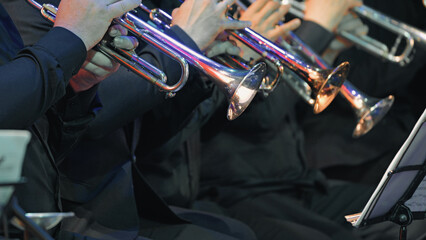 Closeup of symphony orchestra trumpet players in black formal wear. Polished brass instruments reflect stage lights. Hands positioned on valves. Mood is focused professional © VeNN