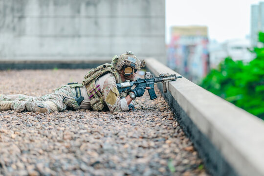 Military tactical team takes firing position behind rooftop cover during urban operation