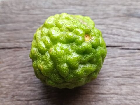 Close-up of organic fresh kaffir lime (bergamot) fruit placed on rustic wood surface. Essential ingredient for Thai cuisine, natural herbal cosmetics, and aromatherapy spa treatments.