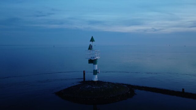 Navigation beacon in the Wadden Sea near West-Terschelling, Terschelling, Friesland, Netherlands, revealing a stone breakwater, calm sea and blue hour sky, drone push-in.