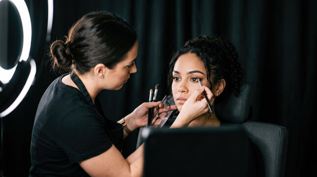 Professional makeup artist applying eyeshadow on a young woman model in a bright studio setting