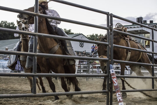 Saint Johns, Michigan, United States - 12 August 2017: View of a rodeo event with horses and riders performing in an arena behind a metal fence.