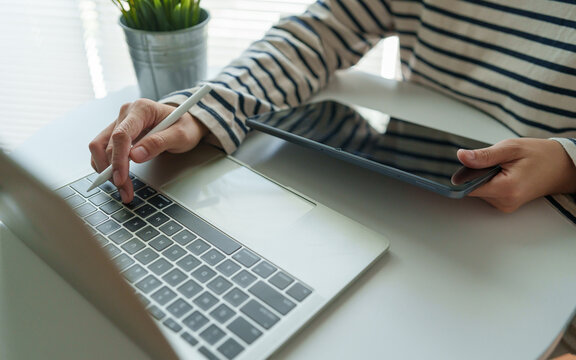 Professional using a tablet with stylus and laptop for multitasking, digital workflow and creative business tasks in a modern workspace.
