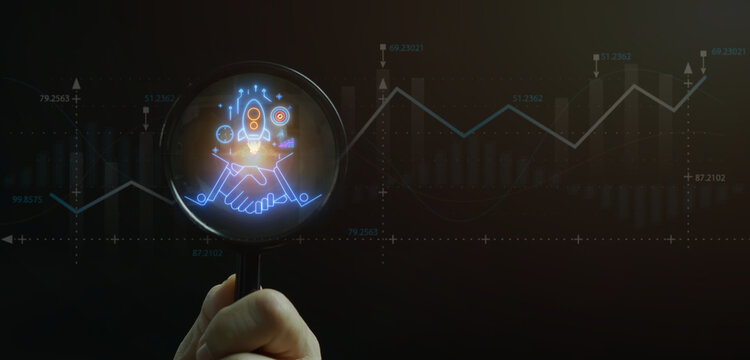 Close-up shot of hand holding magnifying glass to inspect glowing handshake with rocket launch target icon inside. Business partnership agreement audit and startup launch inspection concept.