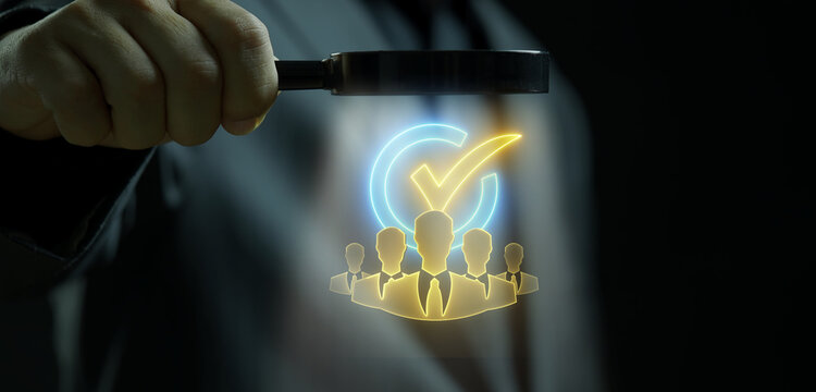 Close-up shot of hand holding magnifying glass to inspect glowing verified checkmark arrow over team profile avatars. Executive workforce recruitment audit and personnel verification concept.