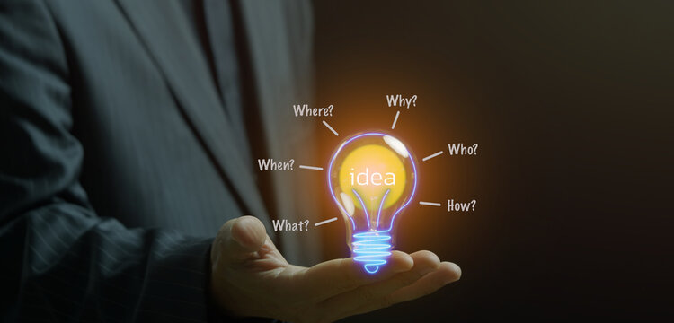 Businessman open hand supporting glowing transparent lightbulb containing Idea text surrounded by question word labels. Creative idea discovery and strategic problem solving innovation concept.