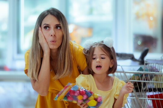 Stressed Mother Looking Confused While Daughter Holds Pompons For Back To School. Tired worried mom stands with excited child holding colorful crafts during school shopping