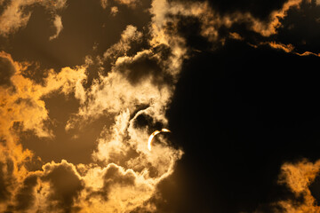 Crescent sun appearing through golden backlit clouds during a partial solar eclipse © Philip