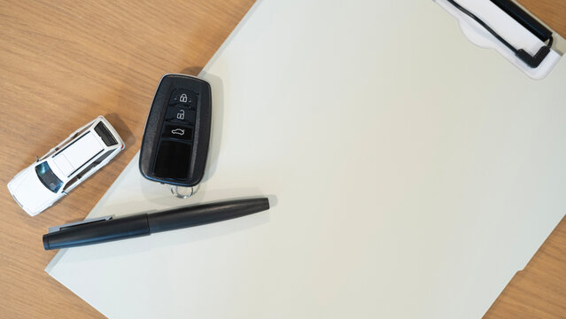 Top view of car key, miniature vehicle and pen on clipboard with blank white background and copy space for text. Concept for car insurance, auto finance, purchase and ownership.