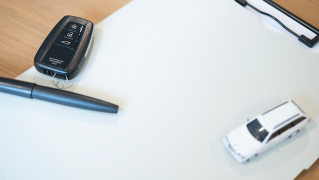 Car key, pen and miniature vehicle arranged around a blank white background with copy space for text. Minimal concept for car insurance, auto loan, purchase and vehicle ownership.