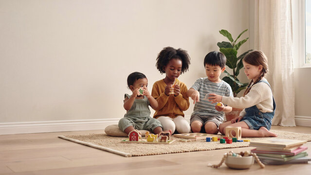 Four diverse children sitting together on a rug and playing with wooden toys.