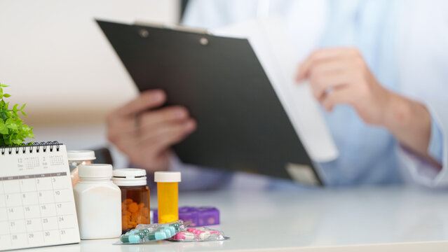 Doctor reviewing medical chart with medicine bottles on desk for healthcare consultation