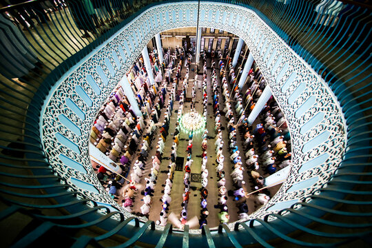 Dhaka, Bangladesh - 20 September 2024: View of the interior of Baitul Mukarram National Mosque with rows of people praying under a large chandelier and ornate blue and white architectural details.
