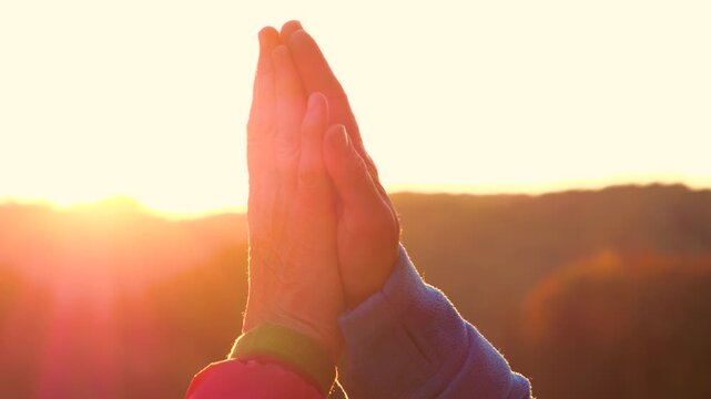 CLOSE UP, LENS FLARE, SILHOUETTE: Two unrecognizable people pressing their hands together in a high five against a glowing autumn sunset. Outdoor moment of connection, celebration and shared success.