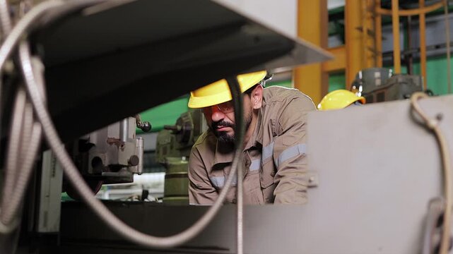 Industrial steelworkers adjusting equipment and operating precise CNC metal cutting machinery on the production line of an engineering parts manufacture factory.