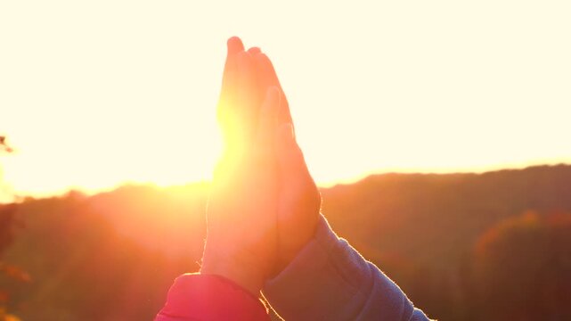 CLOSE UP, LENS FLARE, SILHOUETTE: Two adult people give each other high five as low sun shines between their hands. Natural moment of celebration, joy and human connection after autumn hike in nature.