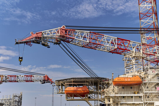 Esbjerg, Denmark - 29 July 2026: View of Wind Enterprise and Bleu Tern wind lift crane ships jacked-up in the harbor with red and white lattice booms against a blue sky.