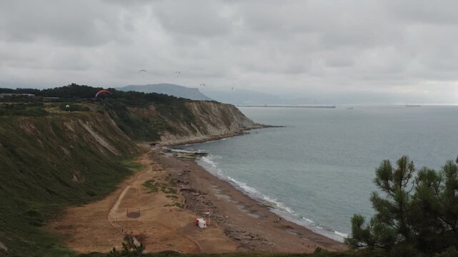 Coastal landscape in Basque Country showing paragliders enjoying the sky above cliffs, beach, and Cantabrian Sea