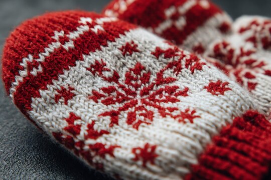 Close-up of red and white knitted mittens with snowflake pattern, cozy winter accessory for cold weather.