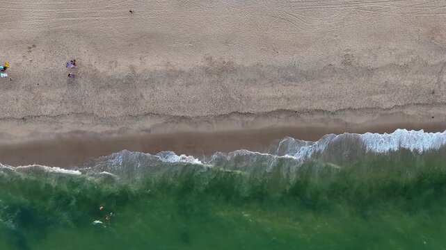 Aerial top-down shot of vibrant green ocean waves breaking on Bay Head Beach with people
