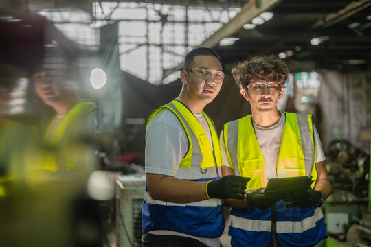 Asian family of father and teenage son in a vintage family metal workshop, framed between dark blurred machine columns, dad holds the tablet low, son's, small family business heritage