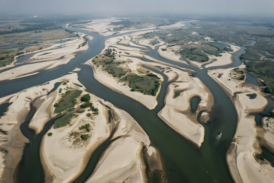 A wide aerial view of a sprawling river delta with numerous sandbanks and small islands, set in a vast natural landscape under a hazy sky above