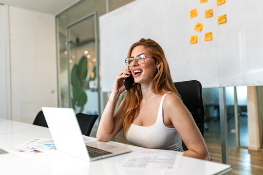 Business call. Office smartphone conversation, Woman talking on mobile phone at desk, Corporate communication concept. Smiling female employee communicating on smartphone in modern workplace.