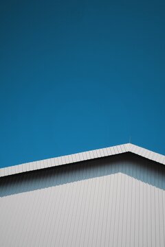 Minimalist geometric composition of a stark white corrugated metal roof against a vibrant, clear blue sky on a bright day