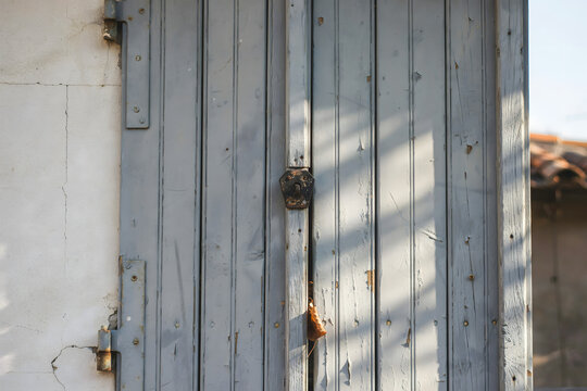 Close-up of aged light blue wooden window shutters with a dark metal latch on a textured white wall showing signs of wear and peeling paint