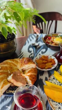 Healthy oriental brunch table setting with delicious Turkish menemen in copper skillet, armudu tea cups and fresh sweet mango. Traditional food styling with ikat patterned tablecloth by a window.