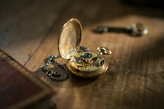 Vintage gold pocket watch with an open lid showing internal clockwork mechanisms placed on a weathered wooden surface with a metal key nearby