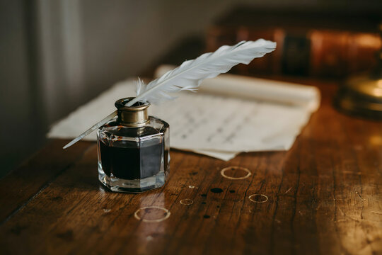 Vintage writing desk scene with a glass inkwell, a white feather quill pen, and aged parchment paper with ink stains on a dark wooden surface