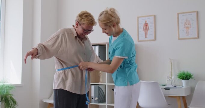 Nurse measures senior patient waist with tape for treatment. Doctor records torso and waist measurement during routine healthcare checkup in medical clinic. Health monitoring, medicine and support.