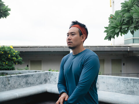 Serious Asian Man in Sportswear and Headband Resting Outdoors in a Modern Urban Landscape