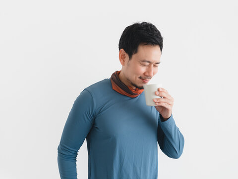 Asian man smiles, eyes closed, savoring the warm beverage's aroma from his mug.