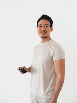 Smiling Asian man holding a small black device, standing against a clean white background.