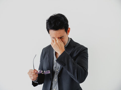 Stressed businessman rubbing his eyes, experiencing headache or fatigue after long work hours.