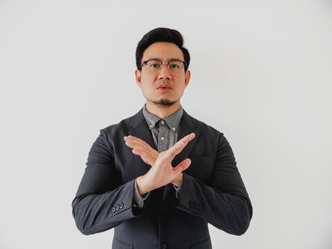Serious Asian businessman making a stop gesture with crossed arms against a white background
