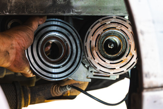 Close-up comparing a new car air conditioning compressor clutch pulley with an old, rusted one during maintenance in an auto repair shop. Automotive repair, spare parts replacement concept.