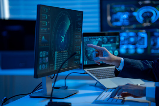 Business person pointing at a flight tracking screen in a modern control room with multiple monitors, laptop, and blue lighting