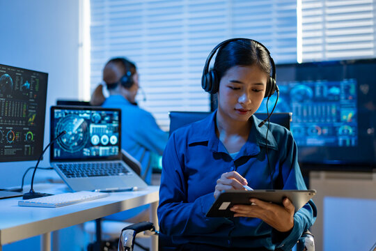 Woman with headset using a tablet in a modern office with computer monitors and a coworker in the background