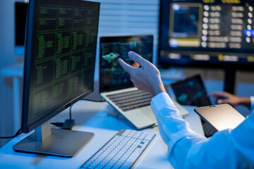 It specialist pointing at monitors with code and data in a modern office, suggesting cybersecurity work, analysis and teamwork. © NanSan