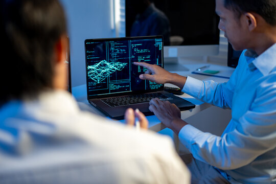 Two professionals reviewing data on a laptop screen in a modern office, with digital charts and code visible during a tech meeting