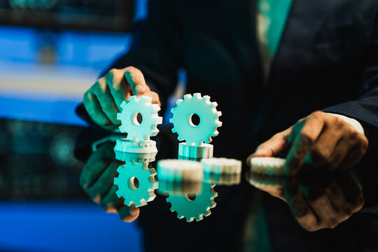 Businessman in a suit arranging white gears on a reflective surface, symbolizing teamwork, planning, and business process