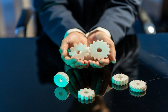 Business person holding white gear wheels above a reflective table, showing teamwork, planning, and process concept