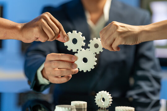 Hands placing white gears together in a teamwork and business collaboration concept with a blurred office background