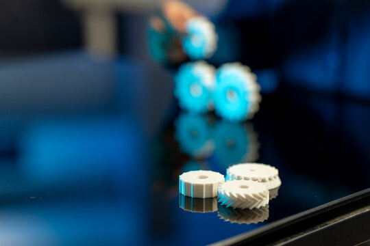Small white plastic gears on a glossy surface with blurred machinery in blue light