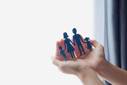 Close-up of hands holding paper cutout of family near window. Concept of family insurance, protection, care, and security.