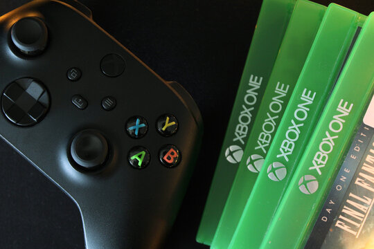 Top view of a black Xbox controller next to green physical game disc cases on a dark background.