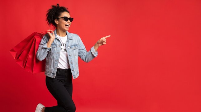 Stylish woman holding shopping bags and pointing at the side in a vibrant studio setting